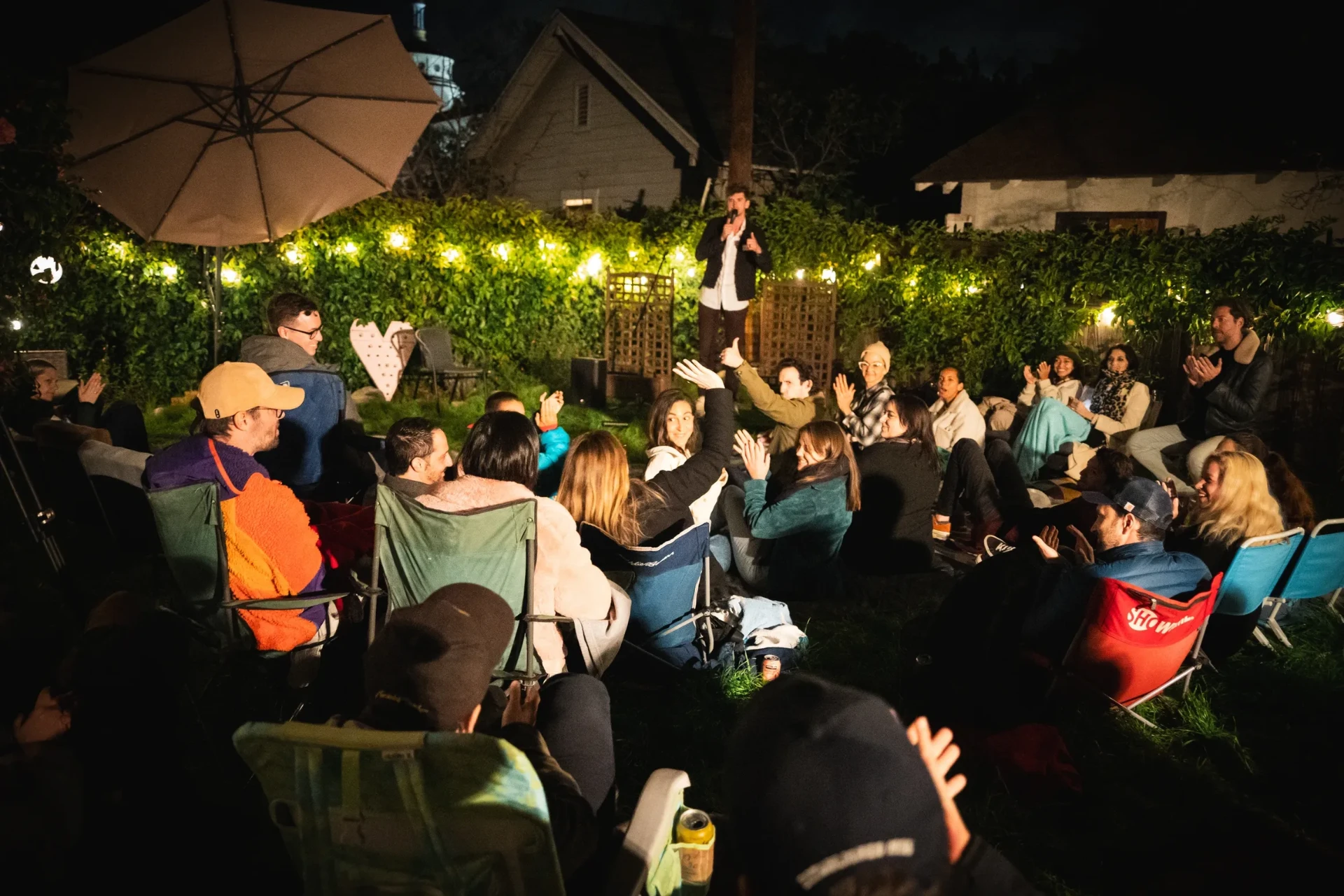 A backyard comedy crowd at night under string lights